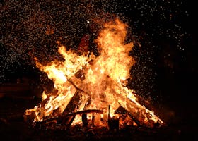 A large bonfire blazing at night with embers and sparks flying into the dark sky.